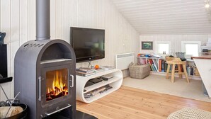 A modern living room with a wood-burning stove, a flat-screen TV, and a cozy seating area with books and a small table. - 8 Person Holiday Home in Nexo-by Traum (Nexø)