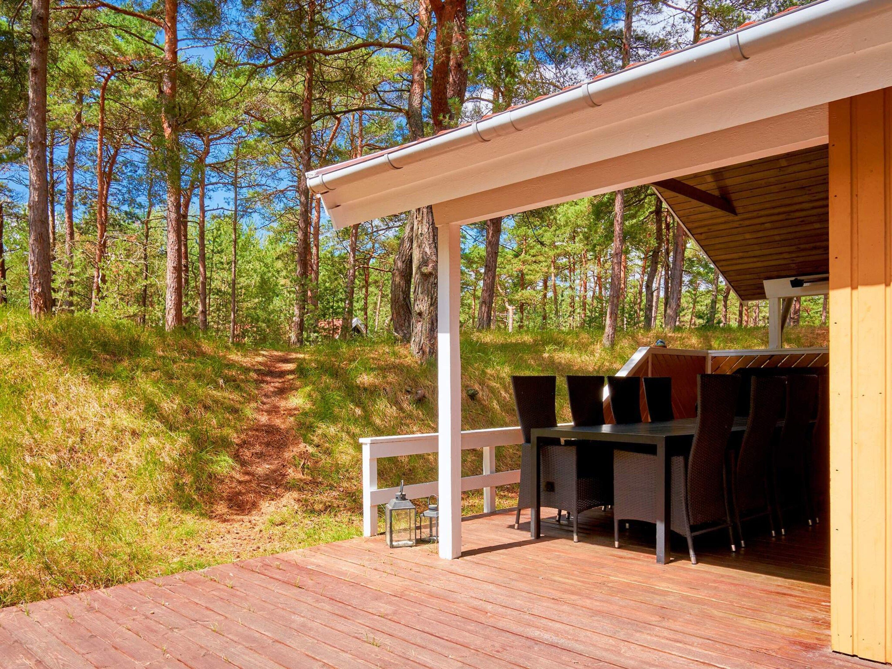 Une terrasse en bois, agrémentée de mobilier d’extérieur, entourée d’une zone boisée.