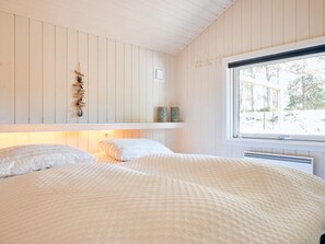 A bedroom with two beds, a window with a view of trees, and a shelf with decorative items. - 8 Person Holiday Home in Nexo-by Traum (Nexø)