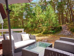 An outdoor seating area with wicker furniture and a glass table, surrounded by a forested landscape. - 8 Person Holiday Home in Nexo-by Traum (Nexø)