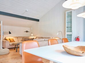 Un salon moderne comprenant un canapé, des fauteuils, une table à manger, des luminaires suspendus et un meuble vitré.