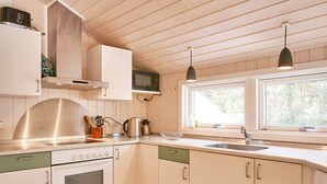 A kitchen with white cabinets, a stainless steel range hood, a microwave, and a window providing natural light. - 8 Person Holiday Home in Nexo-by Traum (Nexø)