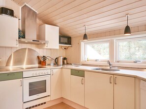Et køkken med hvide skabe, et rustfrit stål emfang, en mikrobølgeovn og et vindue med naturligt lys.