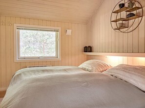 A bedroom with a large window, a bed with a textured blanket, and a wall-mounted shelf with decorative items.