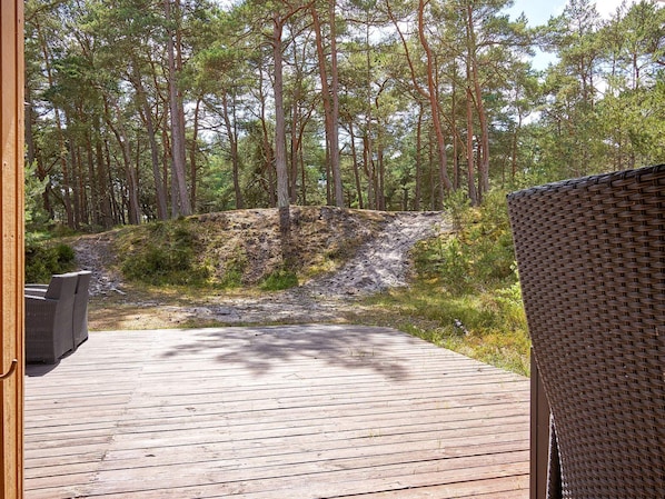 A wooden deck with a wicker chair, surrounded by a forested area.