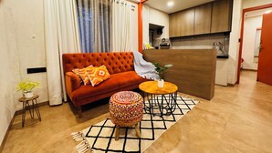 Un salon comprenant un canapé, une table ronde en bois, un pouf à motifs et un tapis.