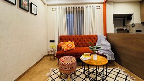 Un salon chaleureux avec un canapé rouge, une table basse en bois et un pouf à motifs.