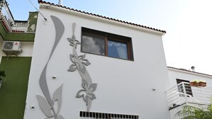 Un bâtiment à deux étages avec une façade blanche, un balcon orné de plantes en pot et une entrée de garage.