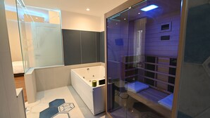 Une salle de bain moderne dotée d’un sauna en verre, d’une grande baignoire et d’un espace douche.