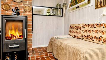 A room with a wood-burning stove, a bed with a patterned headboard, a mirror, and decorative plates on the wall.