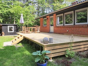 A wooden deck with a table and chairs, a small shed, and a house with a brick exterior and large windows. - 8 Person Holiday Home in Hadsund (Hadsund)