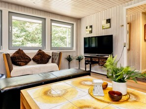 A living room with a sofa, a coffee table, a TV, and a window with a view of trees.