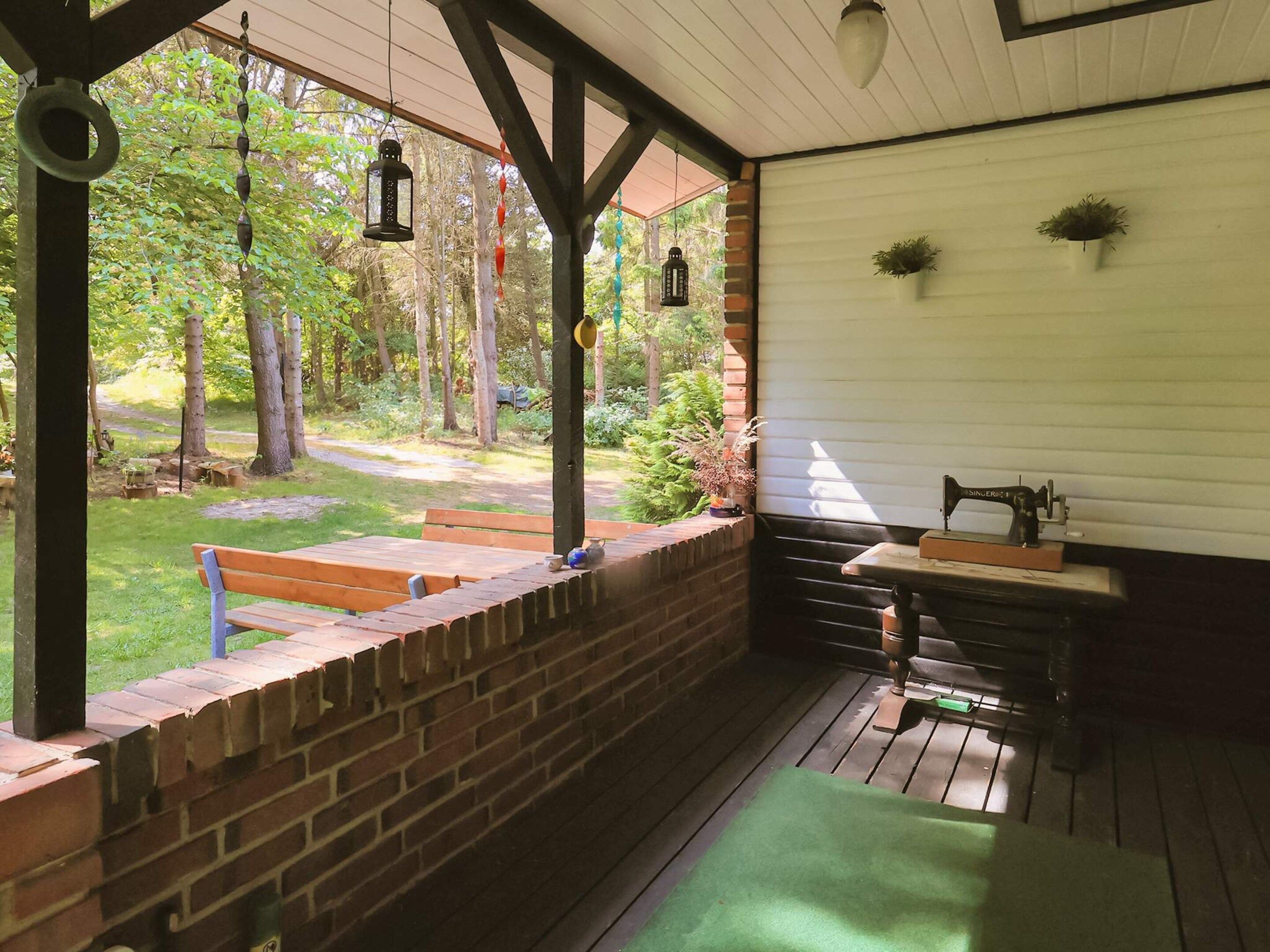 A covered outdoor area with a brick wall, wooden benches, hanging lanterns, and a sewing machine.