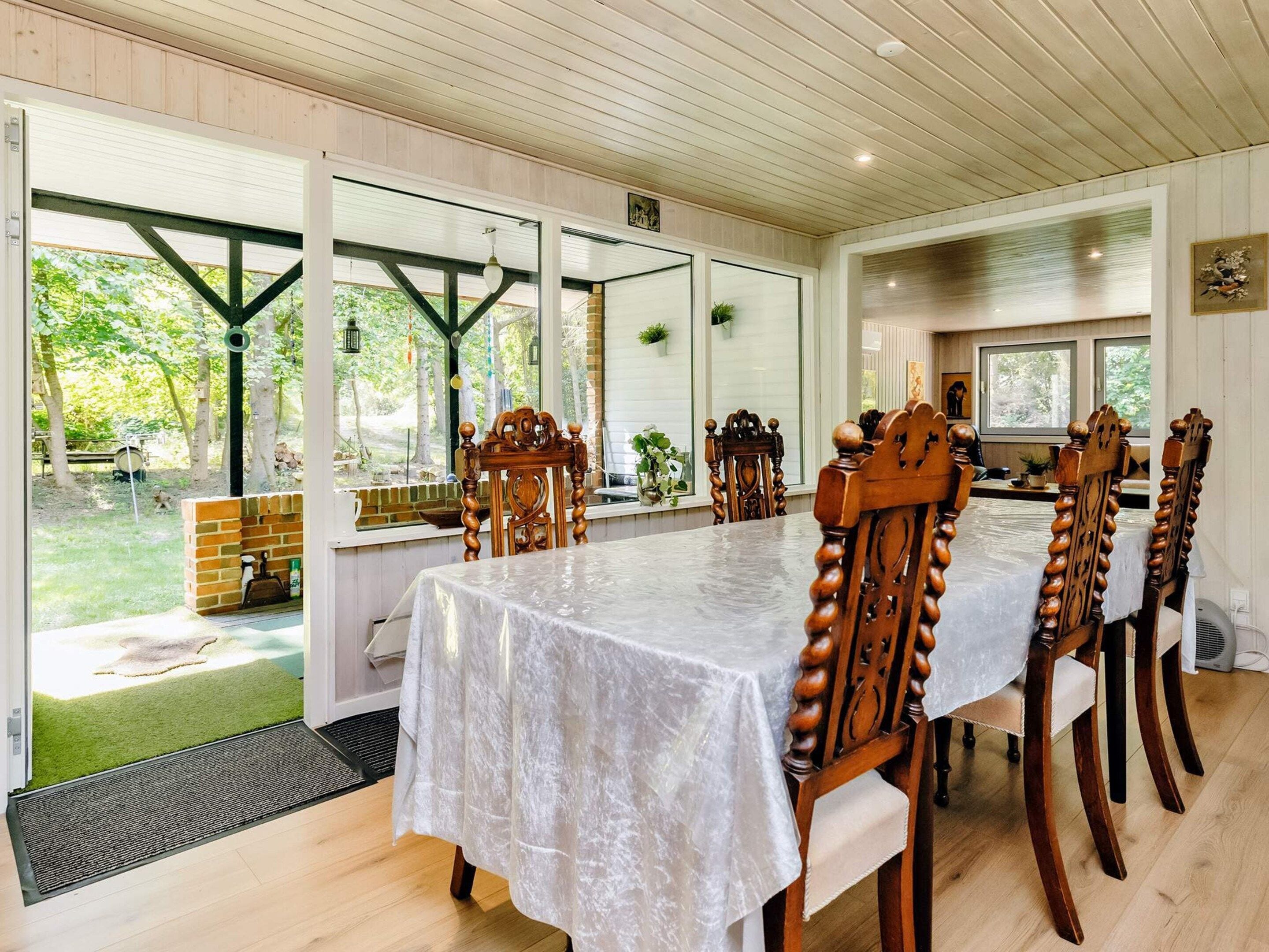 A dining area with a long table, wooden chairs, and large windows.