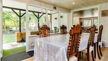 A dining area with a long table, wooden chairs, and large windows.