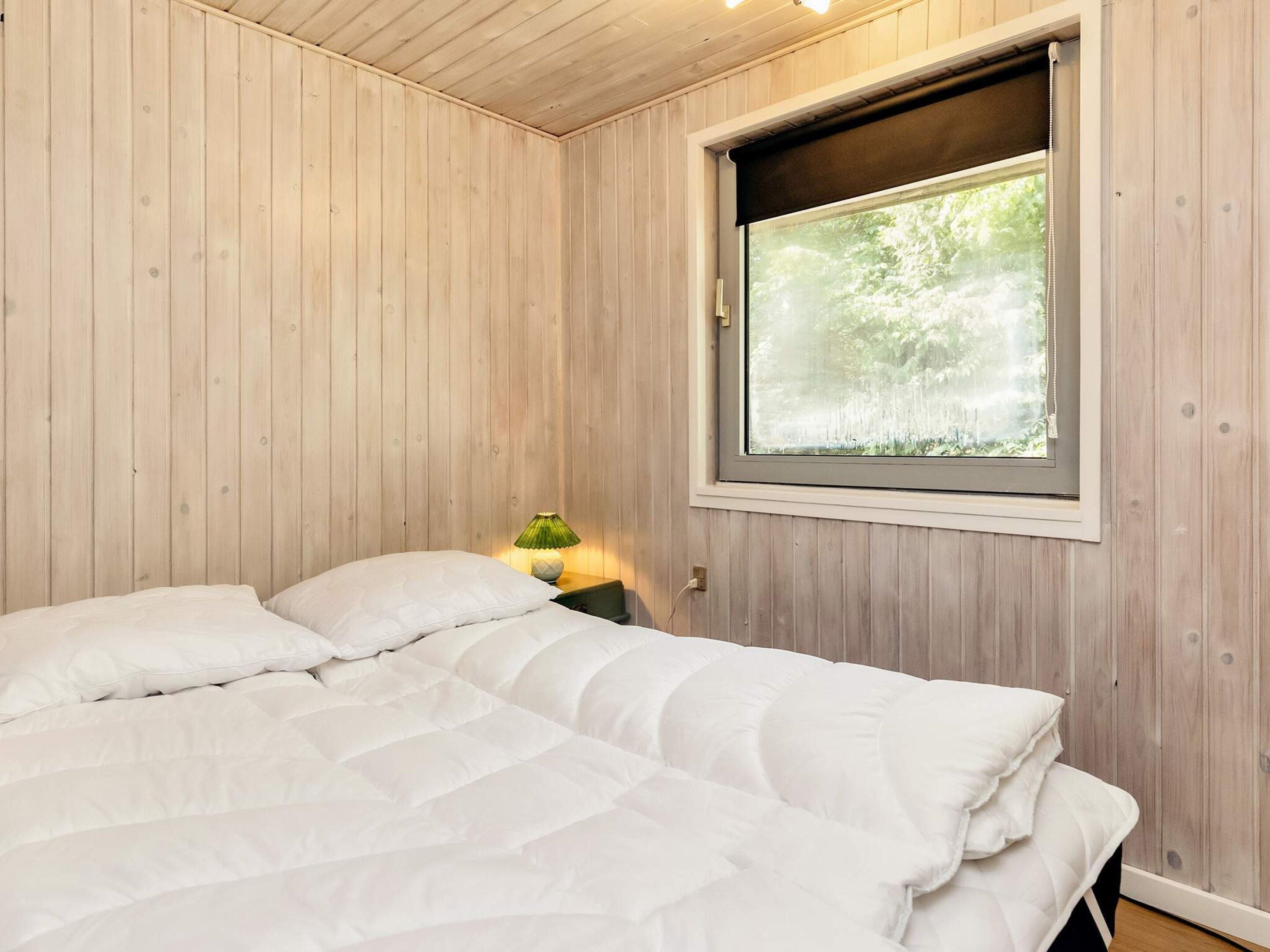A bedroom with a bed, a nightstand, a lamp, and a window with a view of trees.