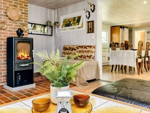 A cozy living room with a fireplace, a dining area with a table set for two, and a kitchen in the background. - 8 Person Holiday Home in Hadsund (Hadsund)