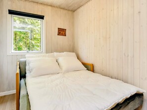 A single bed with a white duvet and pillows, a wooden headboard, and a window with a view of greenery.