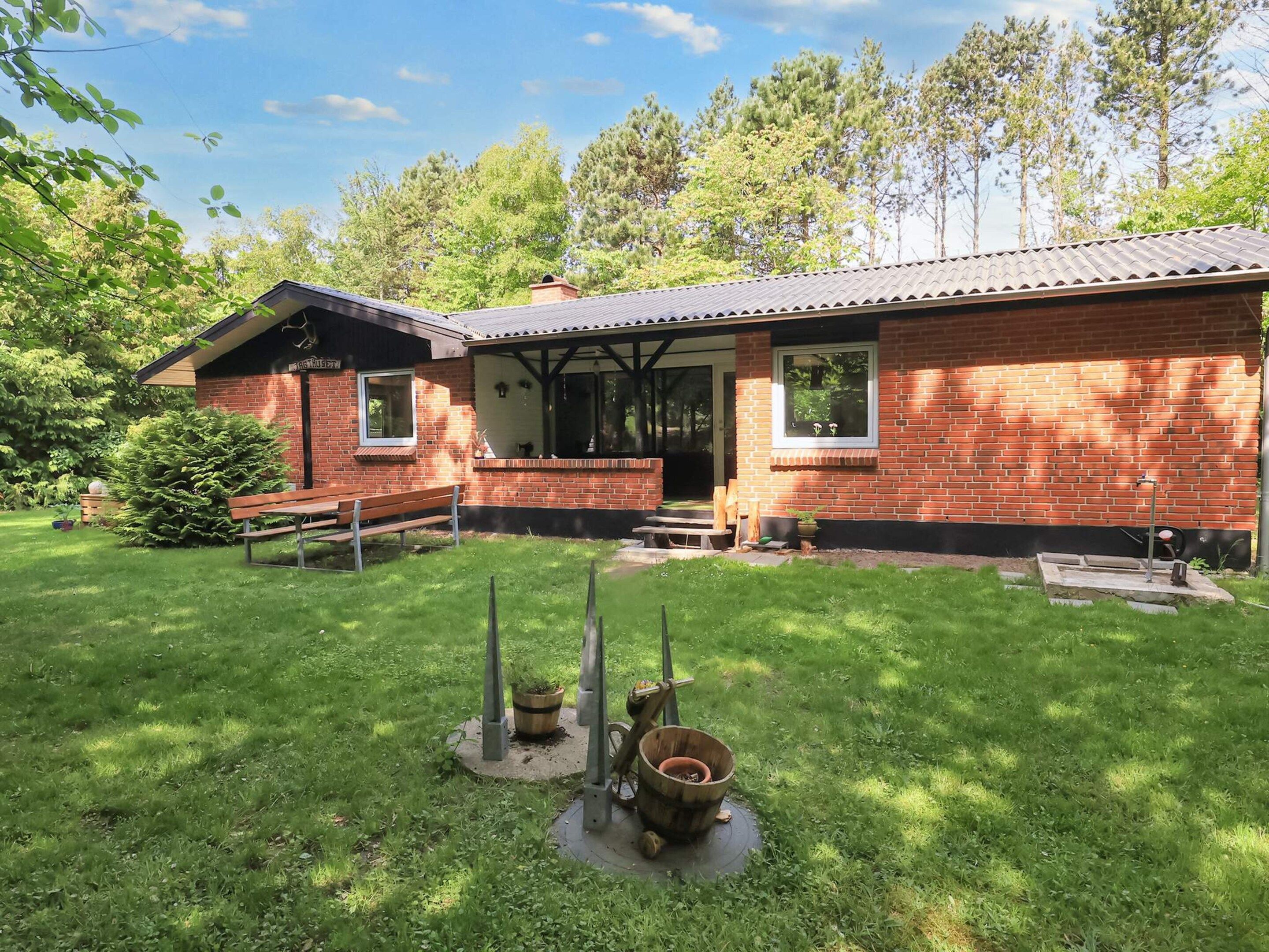 A brick house with a porch, a bench, and a small garden area with a wooden structure.