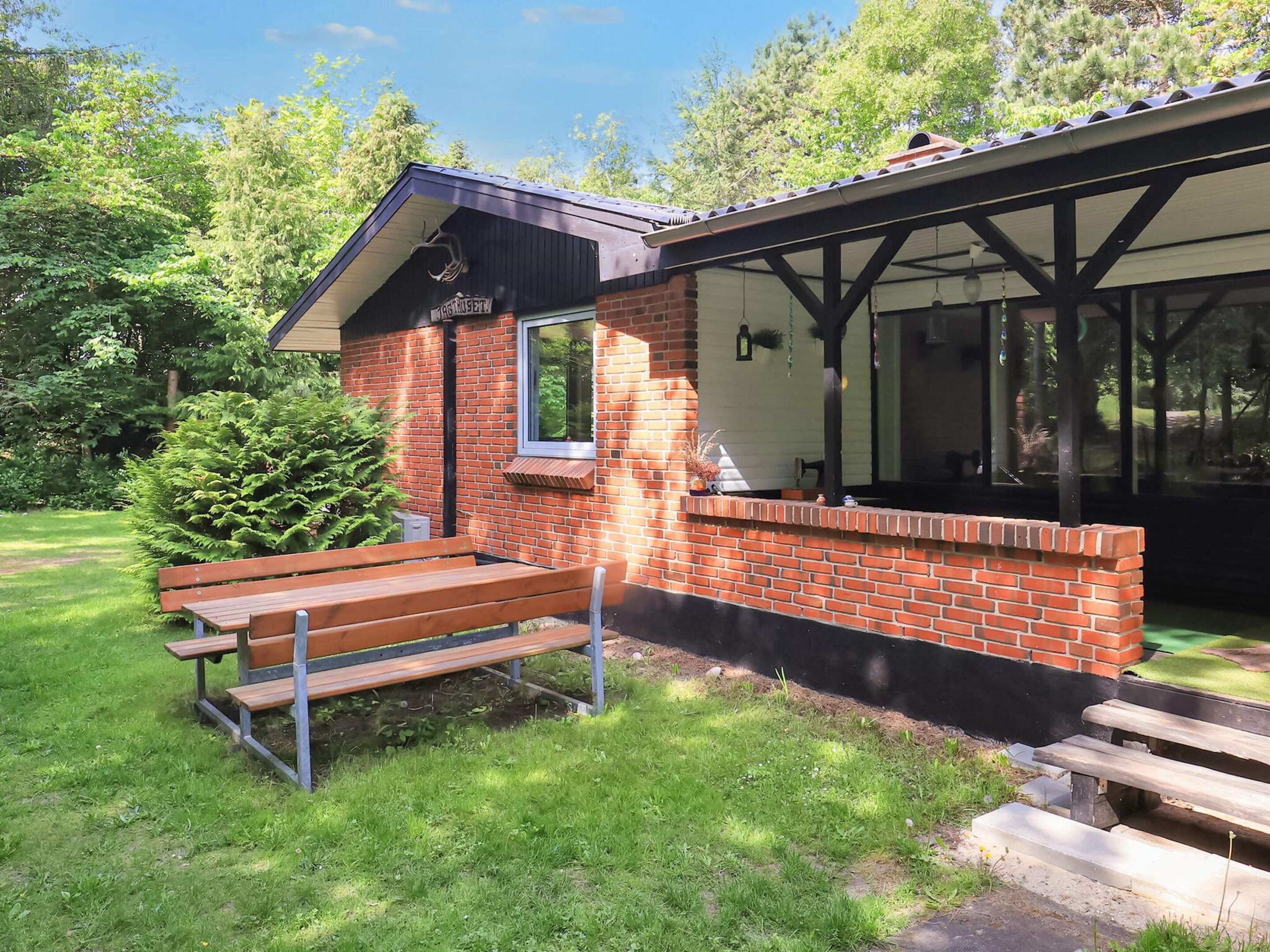 A small brick building with a window and a bench in front.