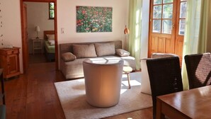 Een gezellige woonkamer met een houten plafond, een bank, een bijzettafeltje en een eethoek met stoelen.