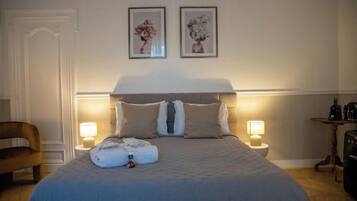 A neatly made bed with a duvet, two pillows, and a folded towel on the bed. There are two bedside lamps on either side of the bed.