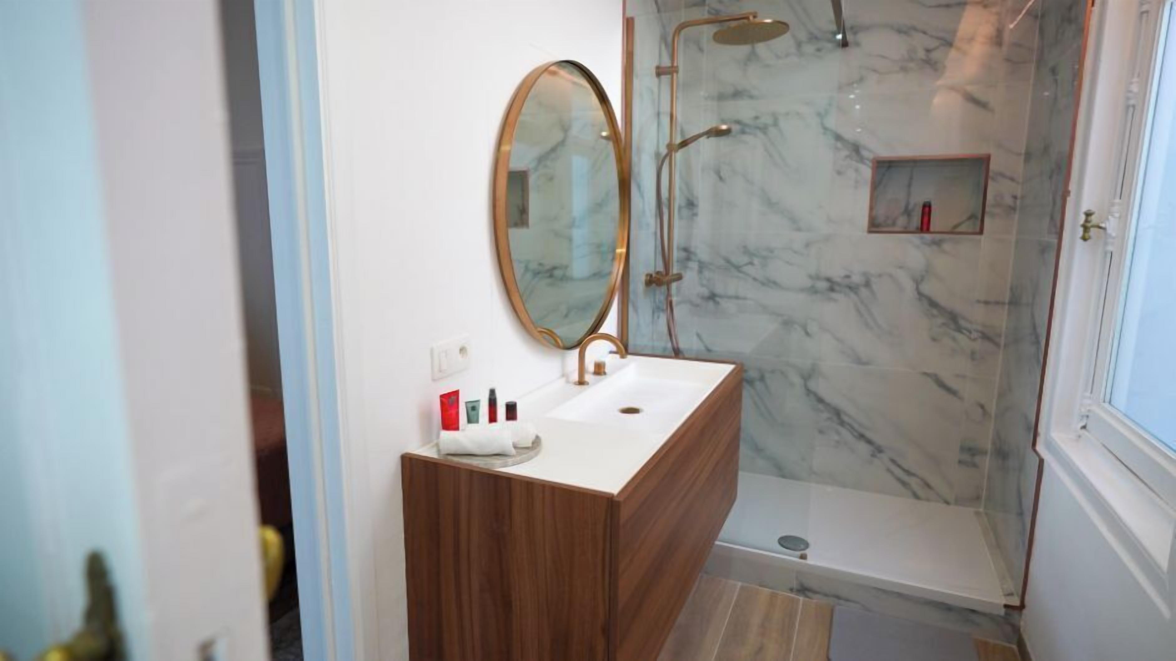 Une salle de bain avec une douche en marbre, un meuble-lavabo en bois et un grand miroir.