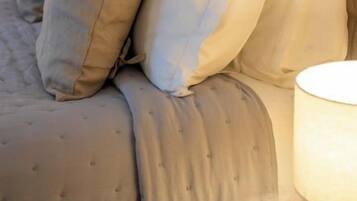 A bed with grey bedding and multiple pillows, a bedside lamp, and a round nightstand.
