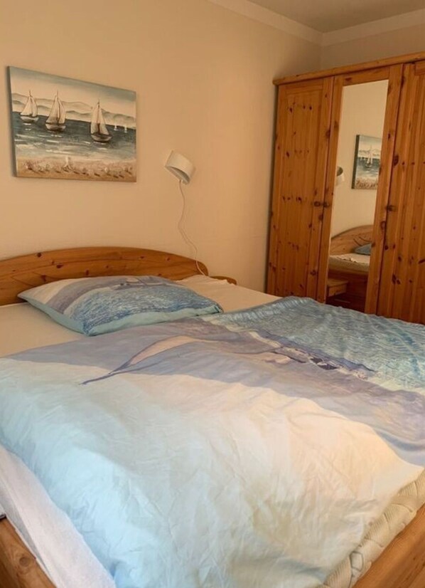 A bedroom with a bed, a painting of sailboats on the wall, and a wooden wardrobe. - Wood in Zempin/usedom (Zempin)