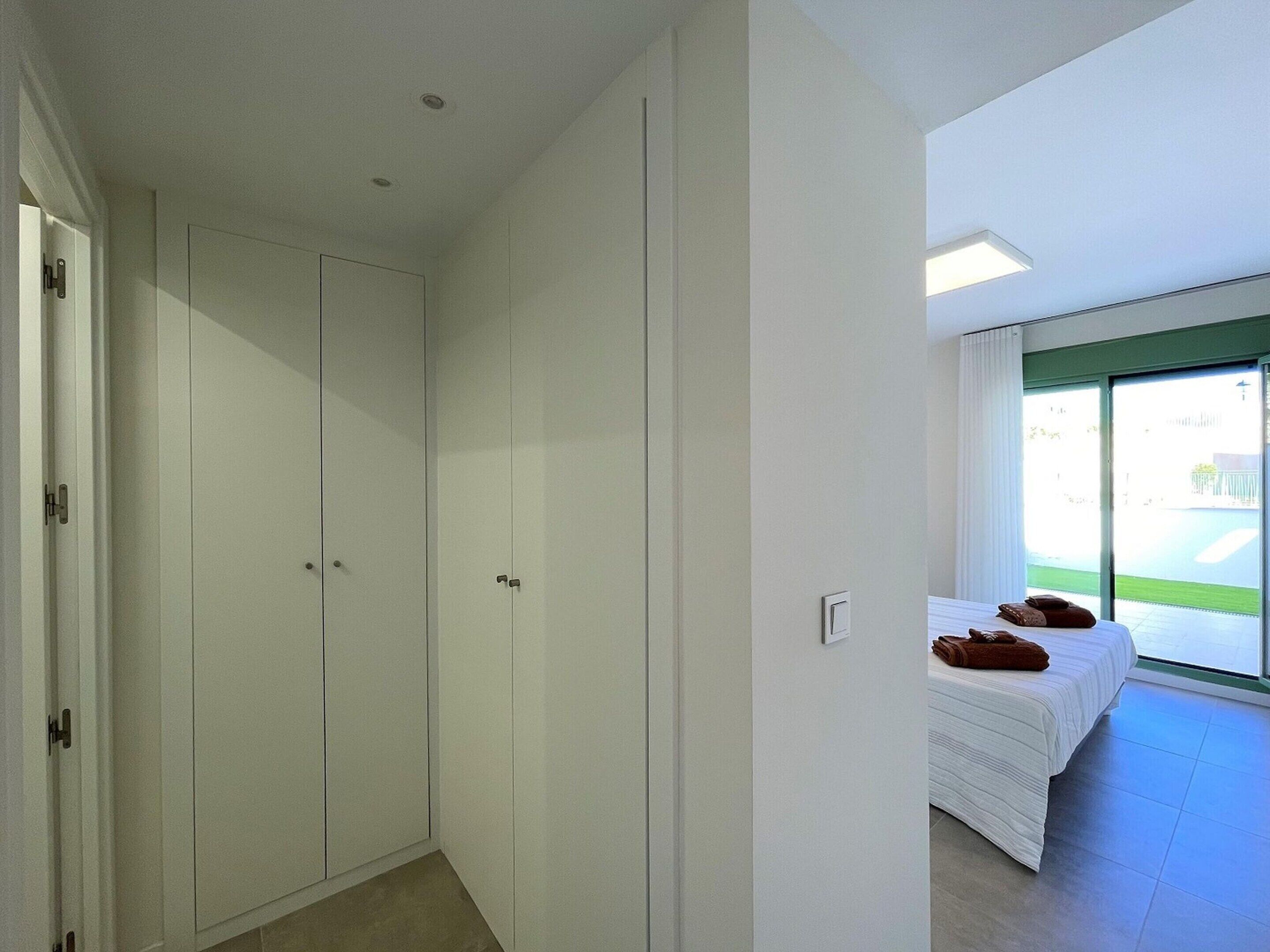 Une chambre dotée d’une grande armoire, d’un lit recouvert d’une couette blanche et offrant une vue sur une pelouse verdoyante par la fenêtre.