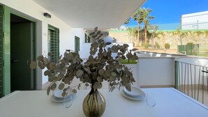 A balcony with a white table, a vase with a plant, and a view of palm trees and a building in the background. - Belvilla by OYO Apartamento Moja!car (Mojacar)