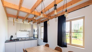 A modern kitchen with white cabinets, a wooden dining table, and a view of a playground through the window. - Holiday Home in Koksijde With Garden (Koksijde)