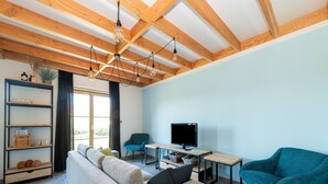 A modern living room with a sofa, a teal armchair, a TV, and a wooden ceiling. - Holiday Home in Koksijde With Garden (Koksijde)