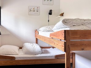 Ein Etagenbett mit weißer Bettwäsche, eine Nachttischlampe und ein an der Wand befestigtes Regal mit einem Buch und einem Paar Schuhen.
