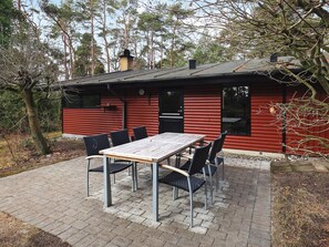 Uma cabana vermelha com um pátio de tijolos, uma mesa e quatro cadeiras.