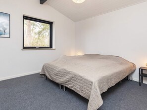 Un dormitorio con una cama grande, una ventana, un cuadro en la pared y una mesita de noche con lámpara.