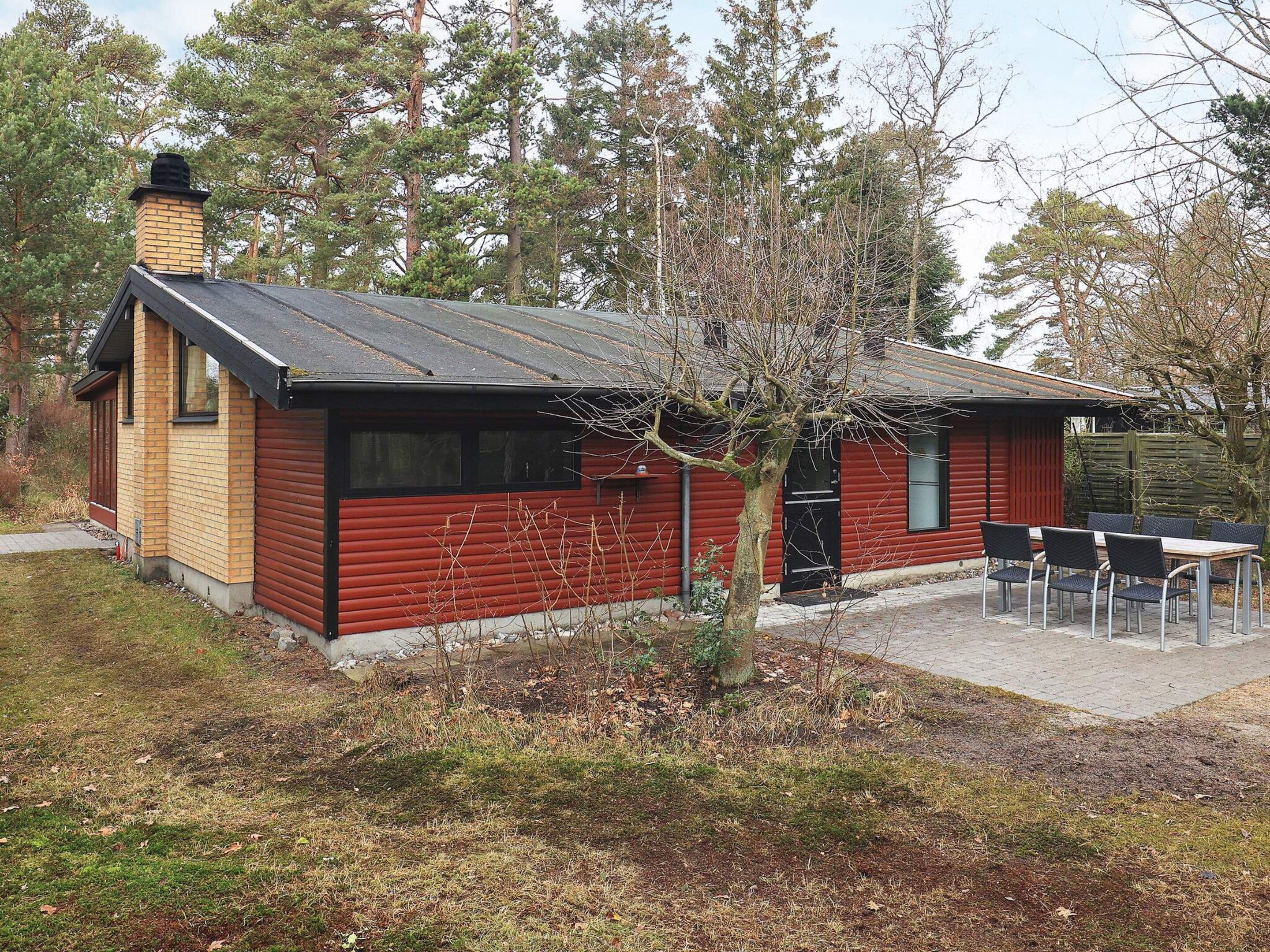 A small, single-story building with a red exterior and a black roof. There is a small patio area with a table and chairs.