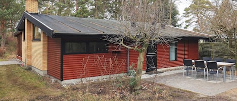 A small, single-story building with a red exterior and a black roof. There is a small patio area with a table and chairs.
