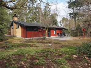 A small, single-story building with a red exterior and a black roof, surrounded by trees and a grassy area. - 6 Person Holiday Home in Vaeggerlose (Vaeggerlose)