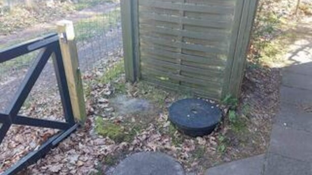 A wooden structure with a metal gate, a circular object on the ground, and a stone slab. - 6 Person Holiday Home in Vaeggerlose (Vaeggerlose)