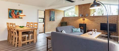A modern living room with a fireplace, a dining area with wooden furniture, and a large window providing natural light.