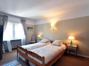 A bedroom with two single beds, a chair, a nightstand with a lamp, a radiator, and a window with curtains. - Gianina Apartment for Five Person in De Haan (De Haan)