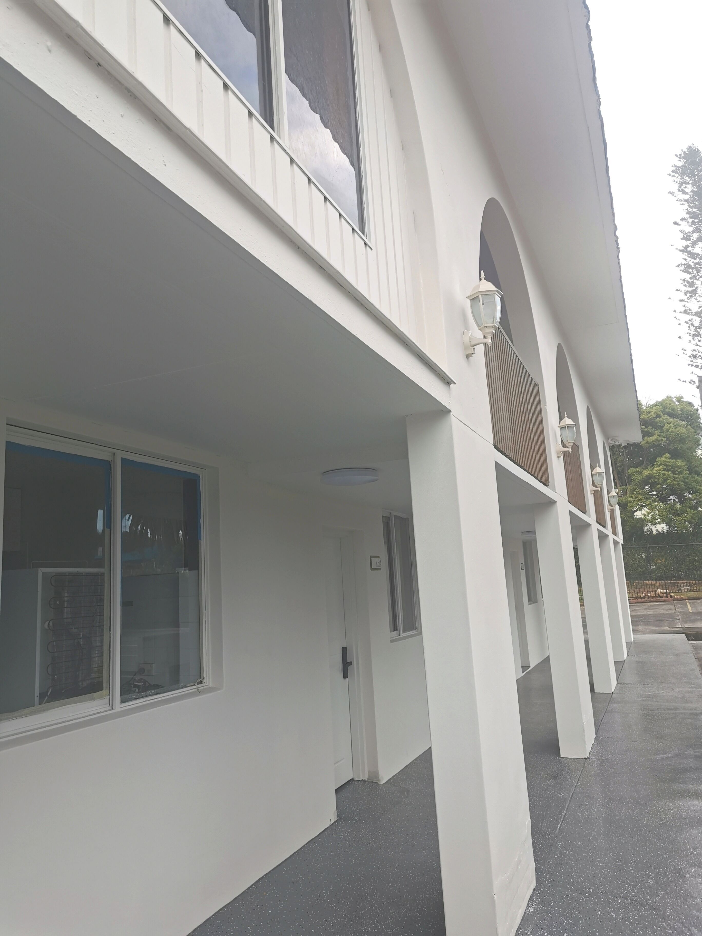 Un edificio con fachada blanca, amplias ventanas y un paseo techado con columnas.