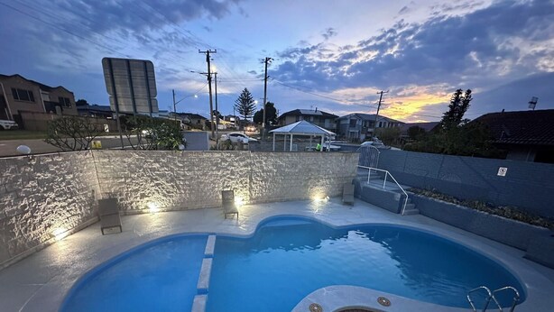 A swimming pool with a wooden deck, surrounded by a stone wall, with a sunset in the background. - Venus Resort (Long Jetty)