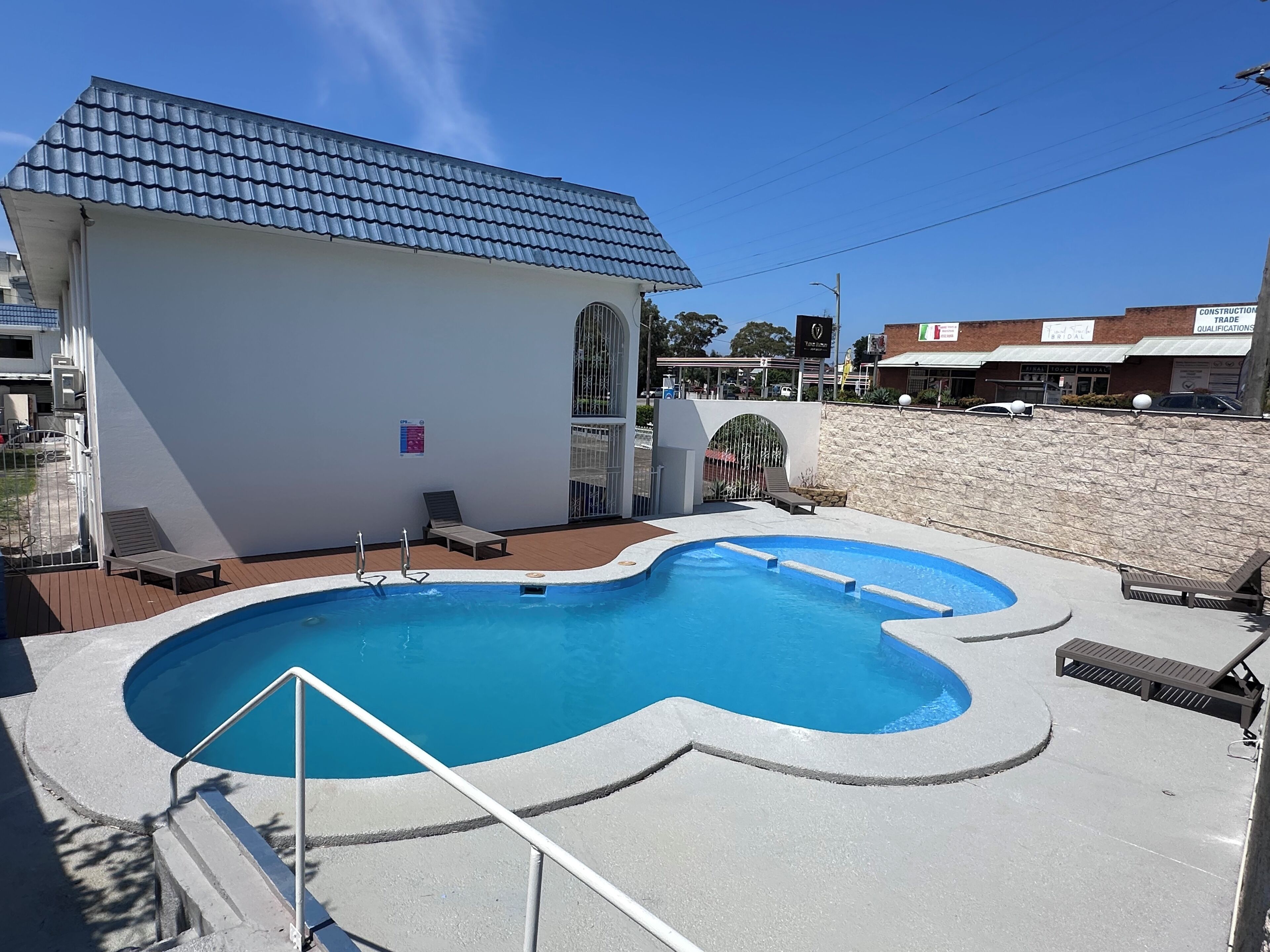 A swimming pool with steps leading into it, surrounded by lounge chairs and a building with a tiled roof.
