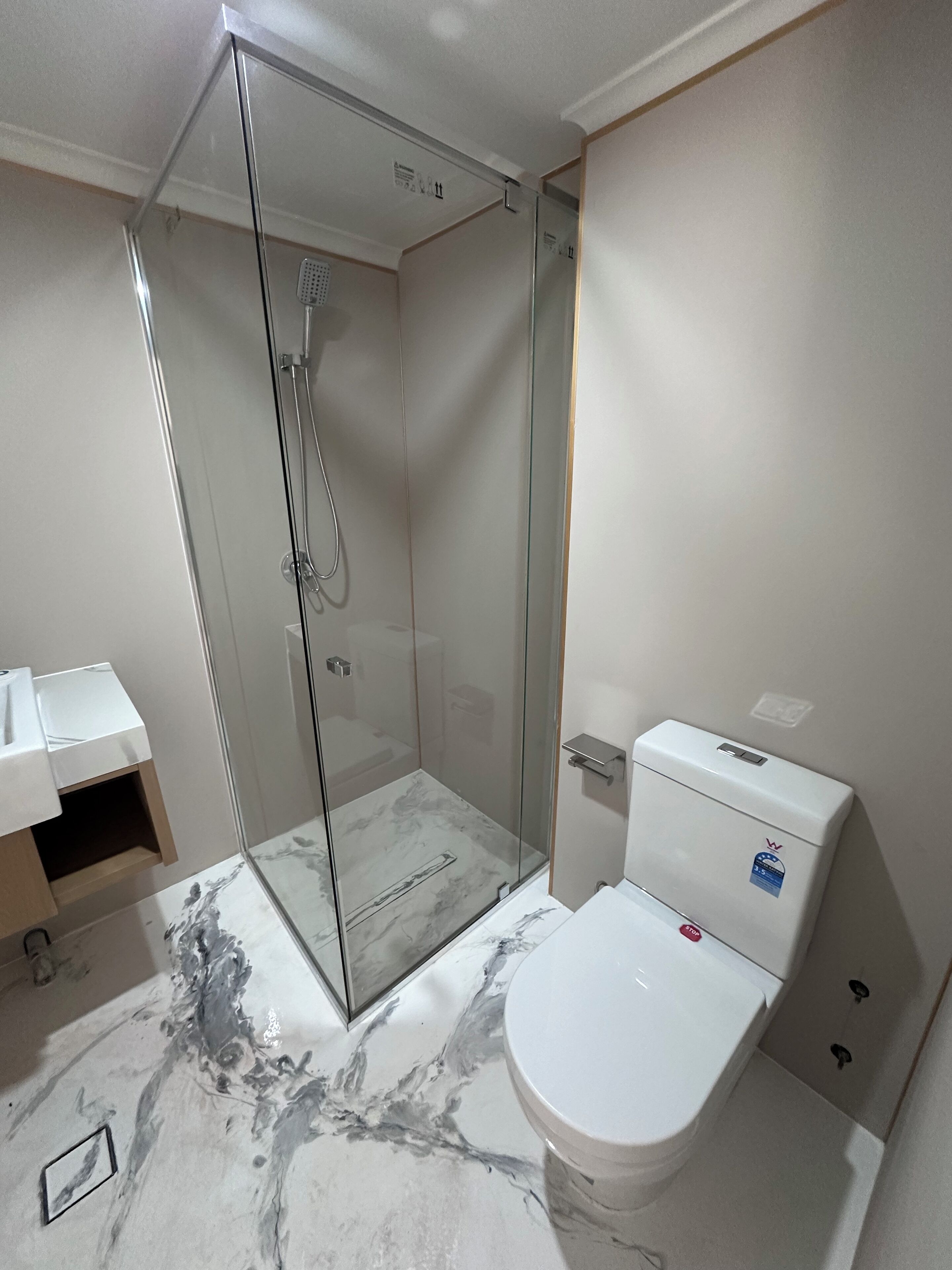 Une salle de bain moderne avec une douche à parois de verre, des toilettes blanches et un sol à motifs de marbre.