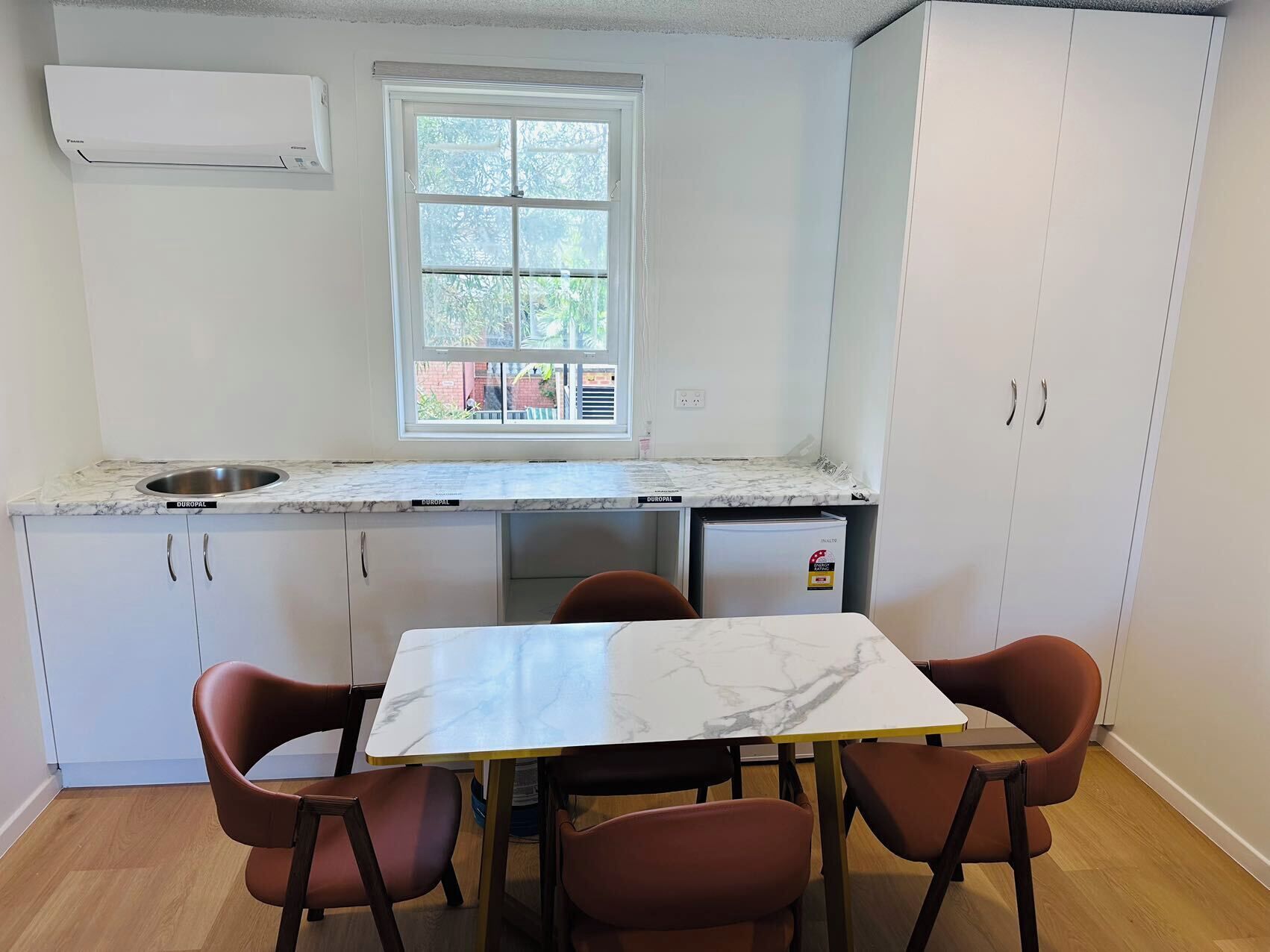 A compact kitchen with a window, white cabinets, a sink, and a dining table with four chairs.
