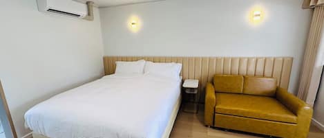 A hotel room with a large bed, a small sofa, and two wall-mounted lights.