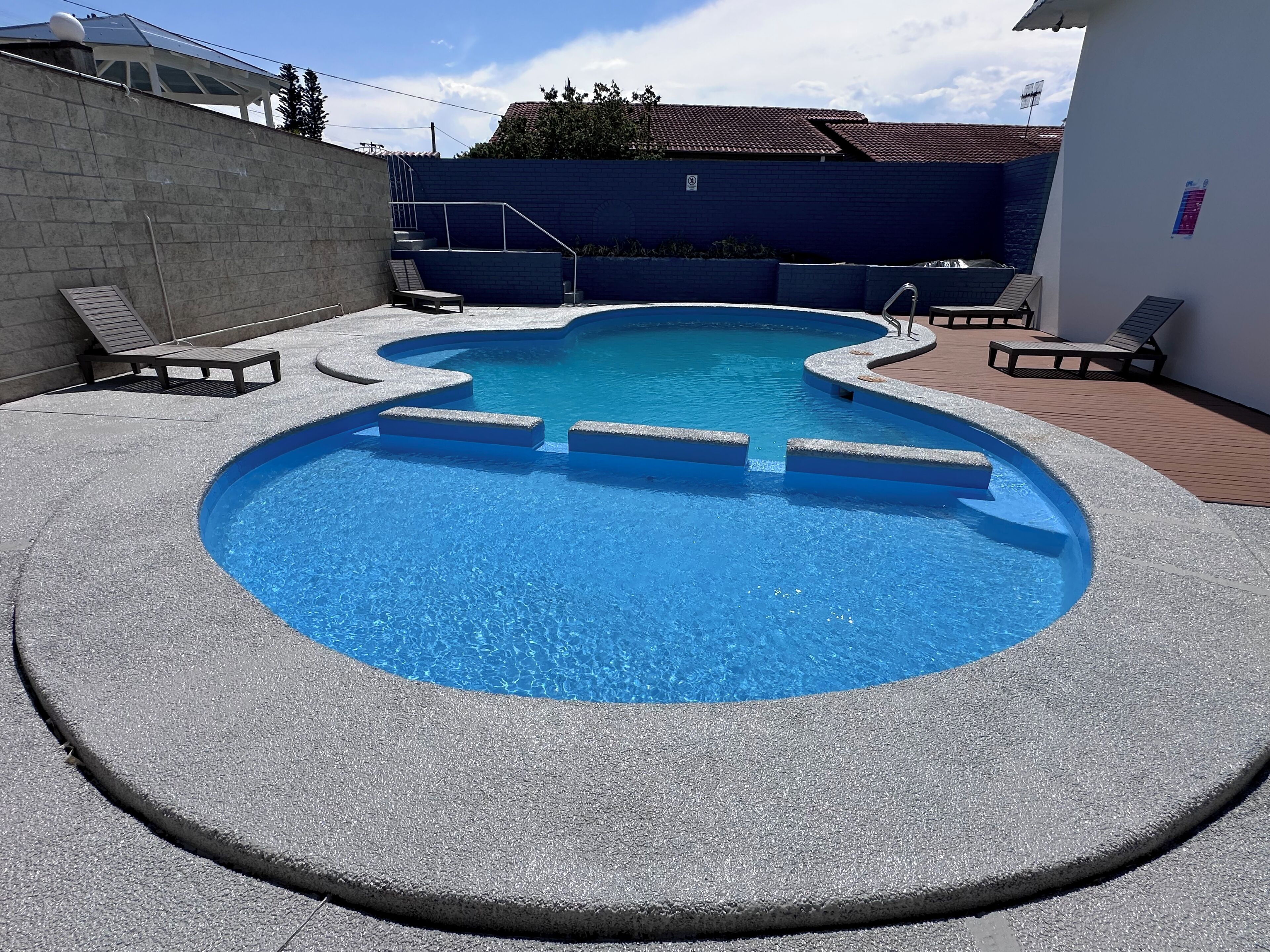 A swimming pool with a unique design, surrounded by lounge chairs and a wooden deck.