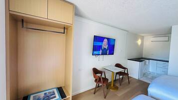 A compact hotel room with a bed, a small kitchenette, a TV mounted on the wall, and a wooden wardrobe.